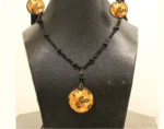 Side view close-up of matching orange floral clay earrings and a larger pendant on black beads.