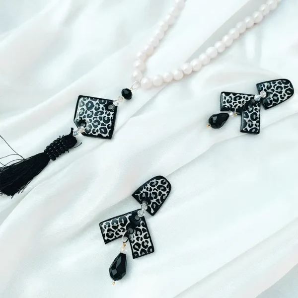 Black Leopard print resin pendant on a white pearl necklace next to matching geometric drop earrings on white silk fabric.