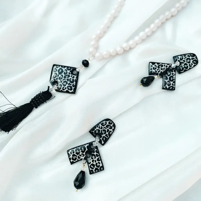 Black Leopard print resin pendant on a white pearl necklace next to matching geometric drop earrings on white silk fabric.