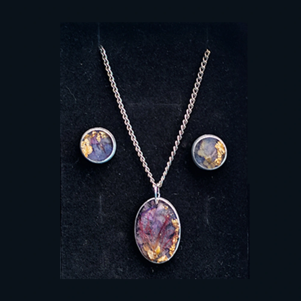 Close-up shot focusing on the oval silver pendant highlighting the intricate purple floral structures and shining gold foil flakes inside the clear resin.