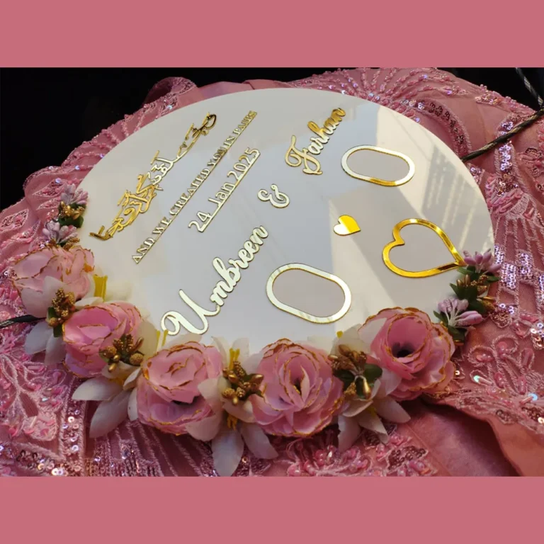 Full view of a round white acrylic thumb impression board with gold lettering and a crescent border of pink flowers.