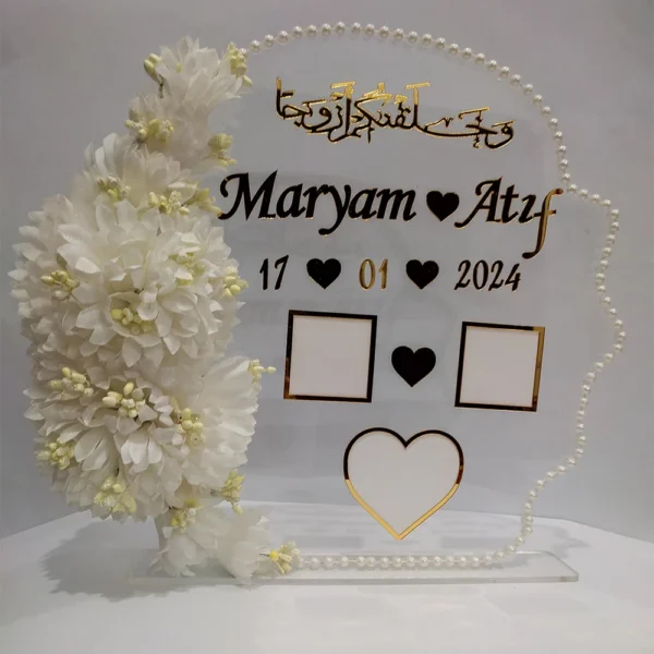Full view of a transparent acrylic thumb impression board with gold lettering and a crescent border of white flowers.