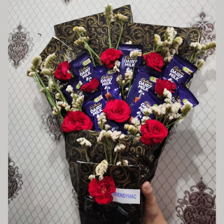 Close-up shot showing the arrangement of Dairy Milk chocolate bars surrounded by bright red roses and delicate white flowers.
