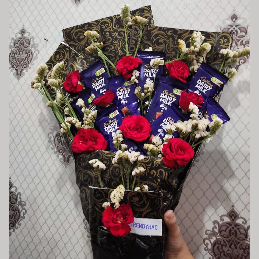 Close-up shot showing the arrangement of Dairy Milk chocolate bars surrounded by bright red roses and delicate white flowers.
