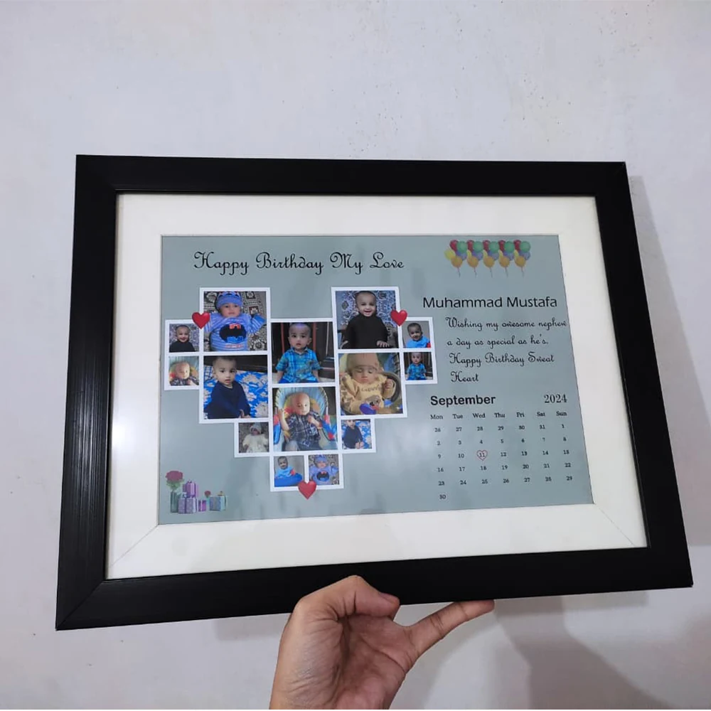 Handheld view of a customized black wall hanging birthday frame with a heart-shaped photo collage and custom text on a green background.