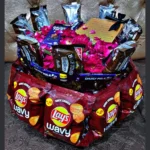 Full view of a multi-layered deluxe snack and chocolate gift tower hamper decorated with festive ribbons.