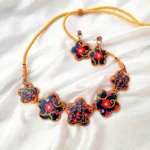 Five flower clay charms linked on a yellow cord necklace with matching earrings on white silk fabric.