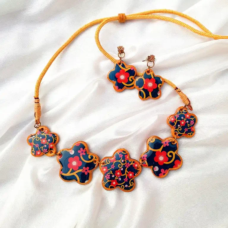 Five flower clay charms linked on a yellow cord necklace with matching earrings on white silk fabric.