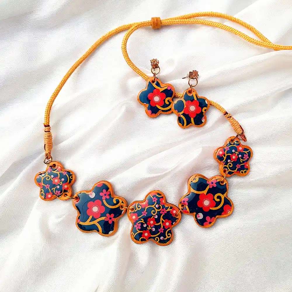Five flower clay charms linked on a yellow cord necklace with matching earrings on white silk fabric.