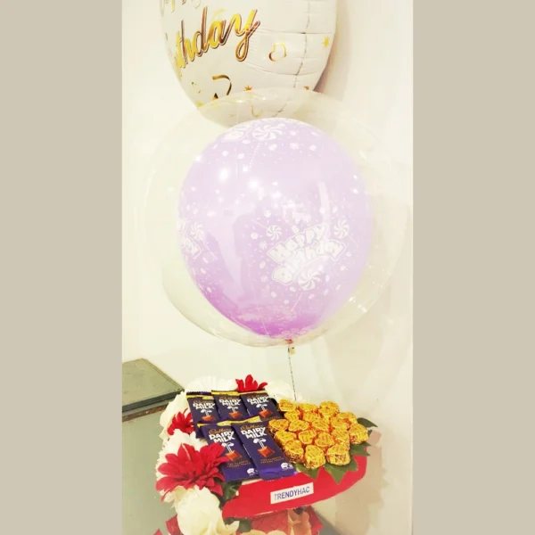 Full view of a heart-shaped chocolate gift basket with a purple happy birthday balloon inside a clear balloon dome.