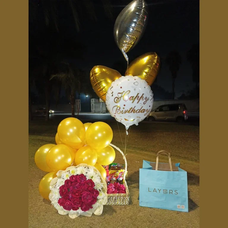 Full outdoor view of a luxury birthday gift basket with gold balloons, a large red rose bouquet, and a Layers cake.