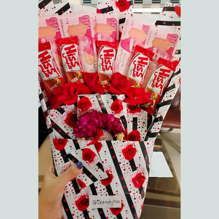 Front view of a money and chocolate bouquet with 100 Rupee notes, Hiss chocolate bars, red roses, and a floral garland.