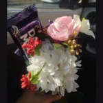 Macro close-up shot focusing on the white and pink artificial flower arrangement and the chocolate bar wrapper.