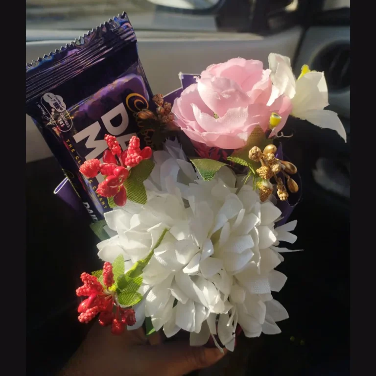Macro close-up shot focusing on the white and pink artificial flower arrangement and the chocolate bar wrapper.