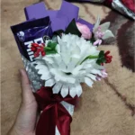 Front view of a mini chocolate bouquet featuring a Dairy Milk bar, a large white flower, and a red ribbon bow.
