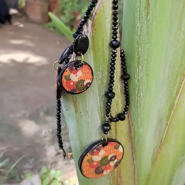Clay floral pendant necklace on a faceted black beaded chain with matching earrings on a green stem.