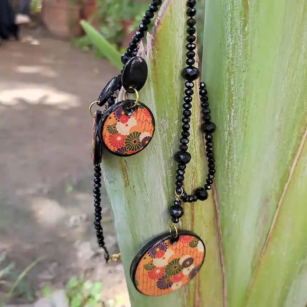 Clay floral pendant necklace on a faceted black beaded chain with matching earrings on a green stem.