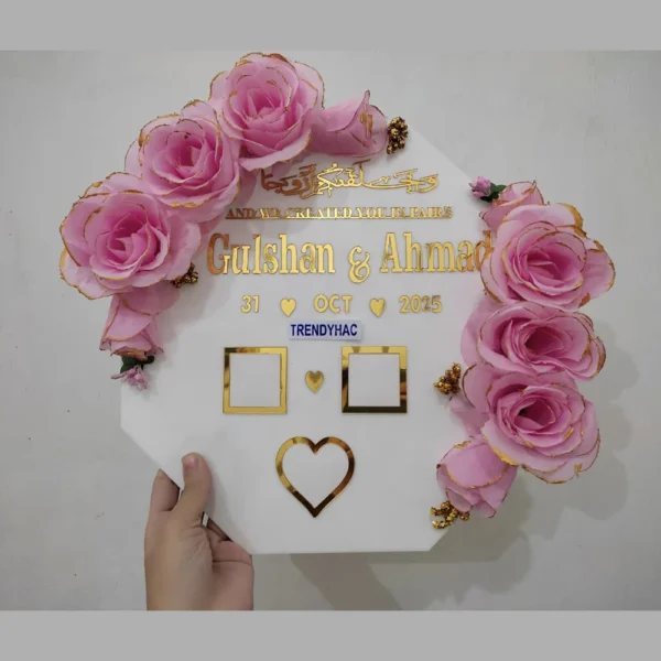 Full view of a hexagonal white acrylic thumb impression board with gold lettering and a crescent border of pink flowers.