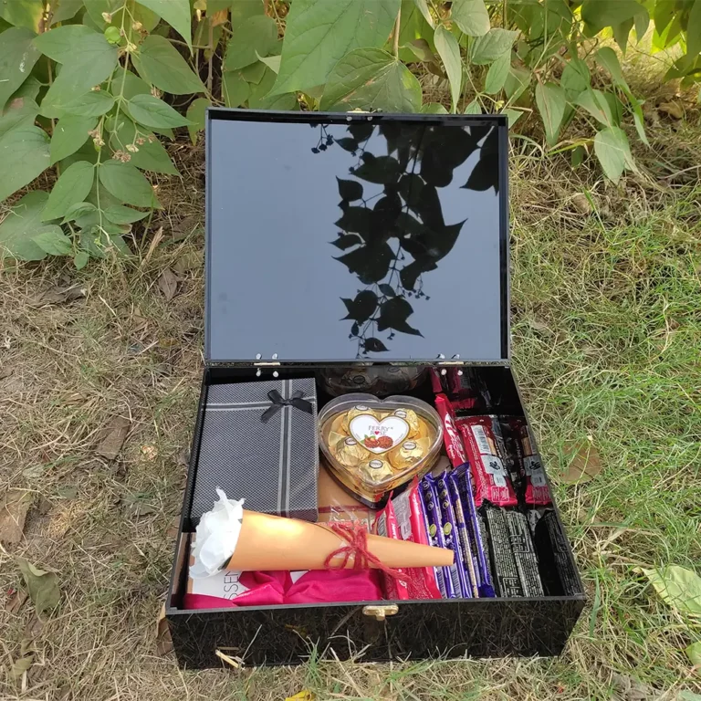 Open black chocolate gift box with assorted jewellery, perfume, letter, flower, chocolates and heart-shaped chocolate pack