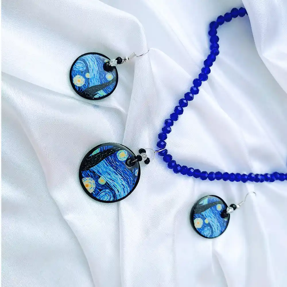 Van Gogh starry night clay pendant on a cobalt blue beaded necklace next to matching round earrings on white silk.