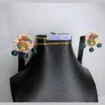 Front studio view of a black display bust showcasing a pair of scalloped cream 3D floral stud earrings with gold roses and dangling dark green beads.
