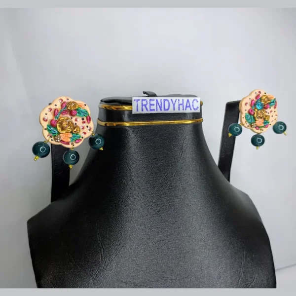 Front studio view of a black display bust showcasing a pair of scalloped cream 3D floral stud earrings with gold roses and dangling dark green beads.