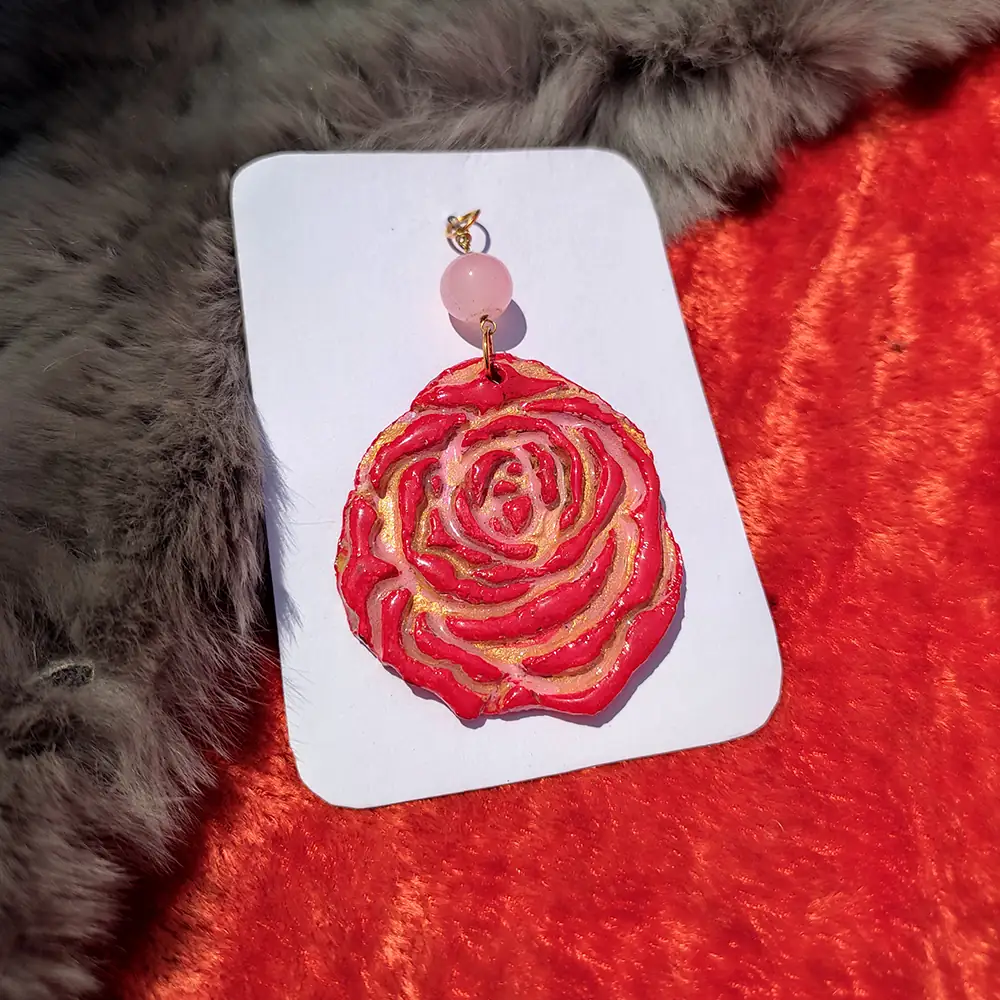 Close-up shot focusing on the sculpted red rose clay petals highlighted with pink accents and shimmering metallic gold paint ridges.
