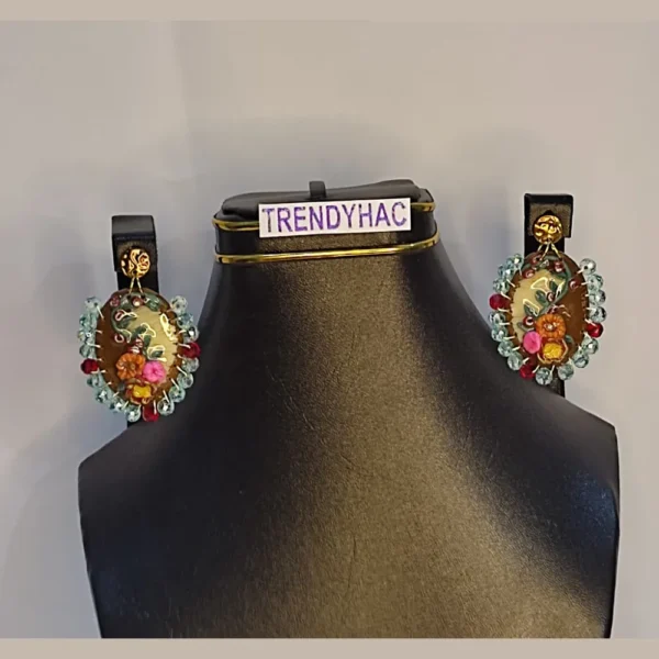 Pair of oval clay floral earrings with sky blue crystal beaded borders displayed symmetrically on a black jewelry stand with a TRENDYHAC label.