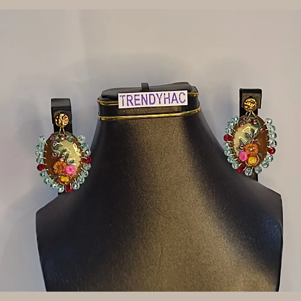 Pair of oval clay floral earrings with sky blue crystal beaded borders displayed symmetrically on a black jewelry stand with a TRENDYHAC label.