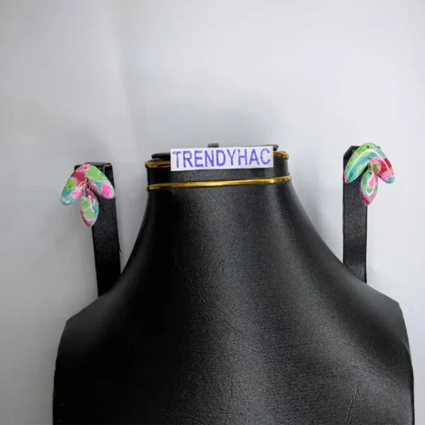 Front studio view of a black display bust showcasing a pair of curved wing-shaped dangle earrings with abstract pink, blue, and green patterns under clear resin.