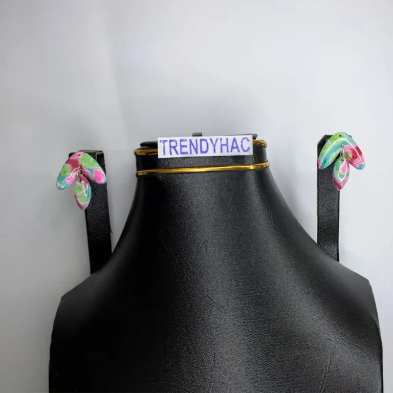 Front studio view of a black display bust showcasing a pair of curved wing-shaped dangle earrings with abstract pink, blue, and green patterns under clear resin.