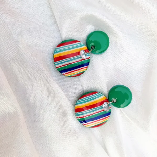 Flat lay view of a pair of two-tier dangling earrings with solid green top studs and multicolored striped bottom discs on white fabric.