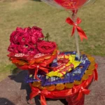Close-up of the red gift base showing arranged Cadbury Dairy Milk bars, KitKats, gold coins, and red roses.