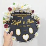 Full view of a round white acrylic thumb impression board with gold lettering and a crescent border of artificial flowers.
