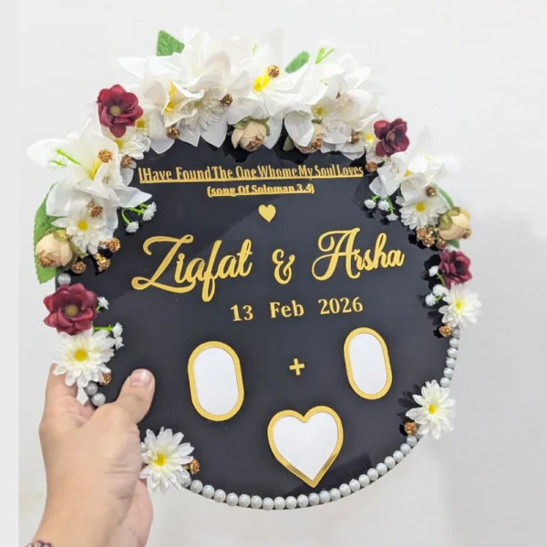 Full view of a round white acrylic thumb impression board with gold lettering and a crescent border of artificial flowers.