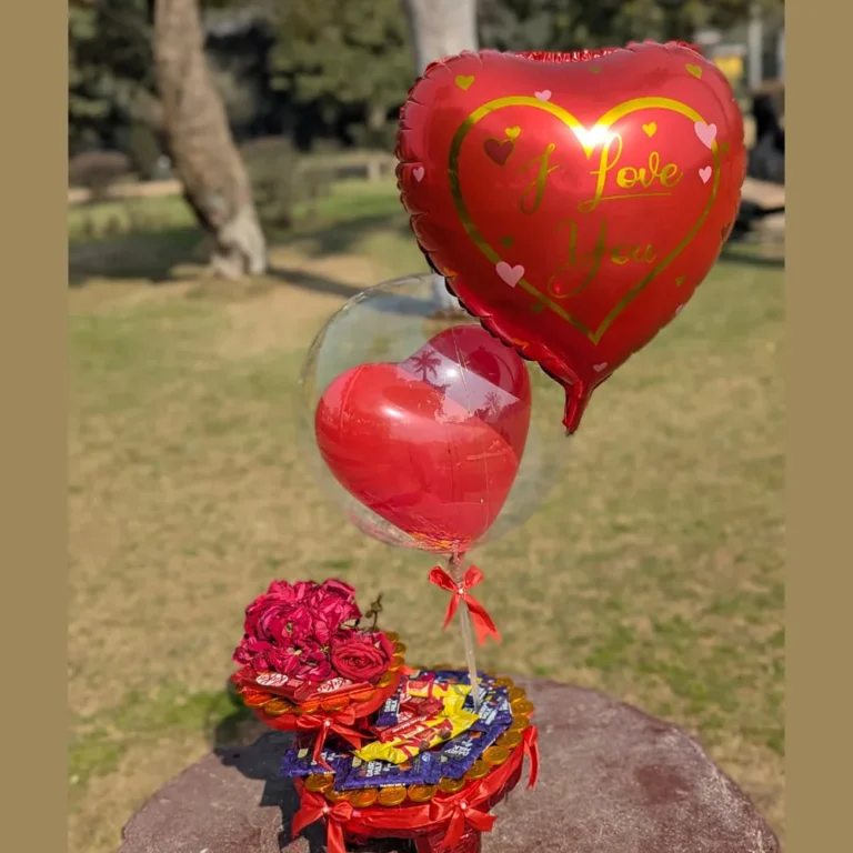 Full view of a multi-tier Valentine's chocolate stand with red roses, a clear heart balloon, and a red I Love You foil balloon.