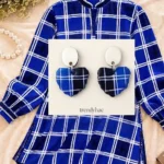 Heart-shaped clay drop earrings with a royal blue, navy, and white plaid pattern on a white trendyhac card, displayed over a matching blue check patterned shirt.