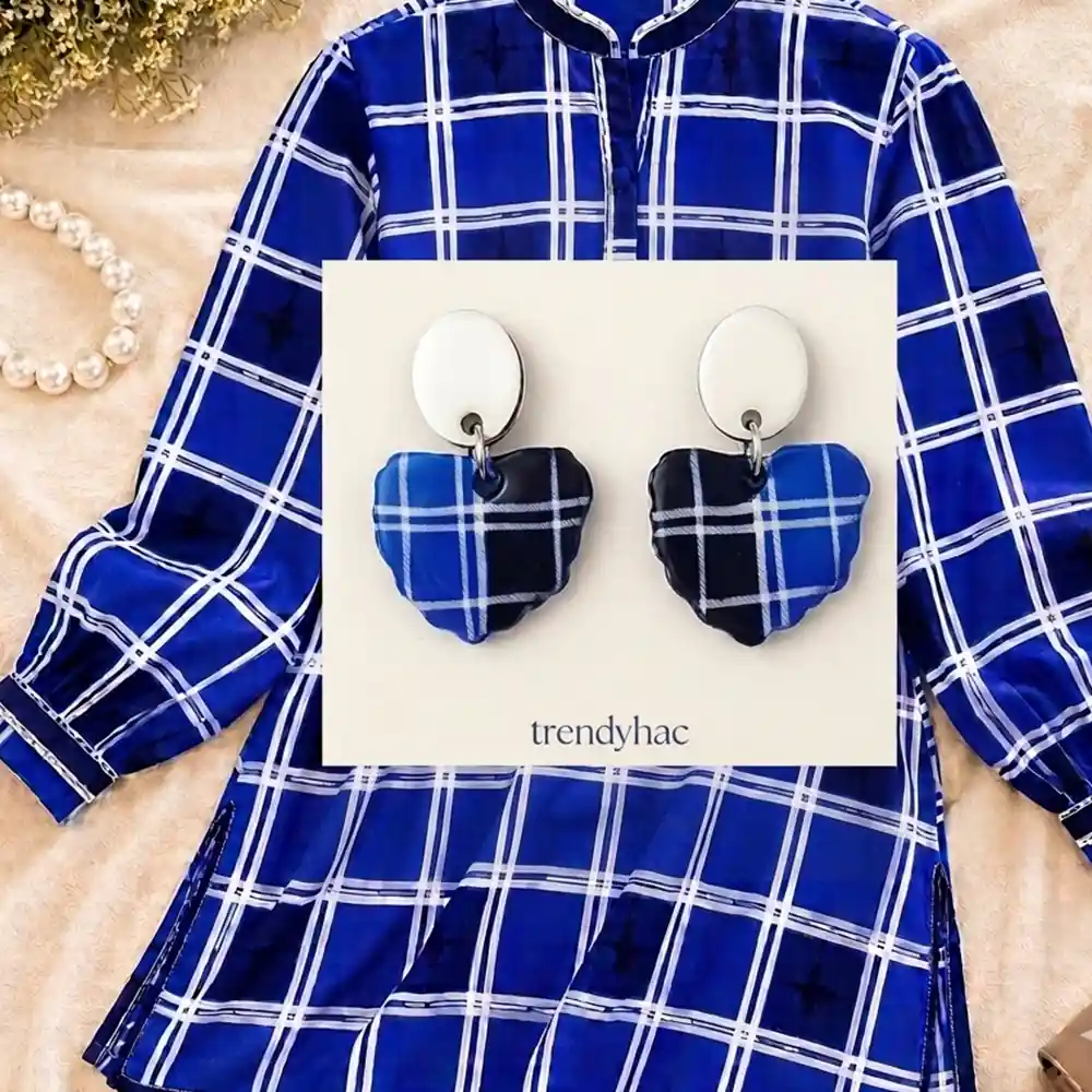 Heart-shaped clay drop earrings with a royal blue, navy, and white plaid pattern on a white trendyhac card, displayed over a matching blue check patterned shirt.