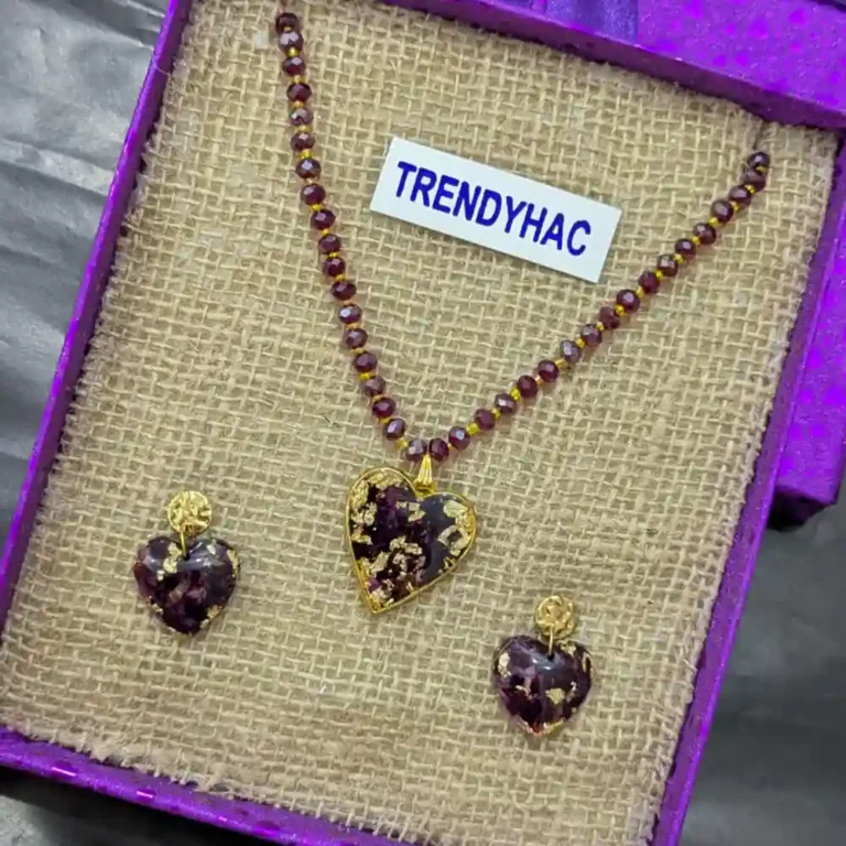 Preserved red rose petal heart pendant on a beaded necklace beside matching drop earrings in a purple box.