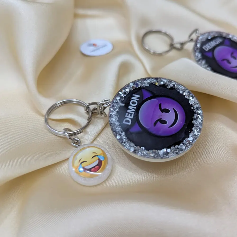 Angled view of a purple demon emoji resin keychain showcasing silver glitter border and laughing emoji charm.