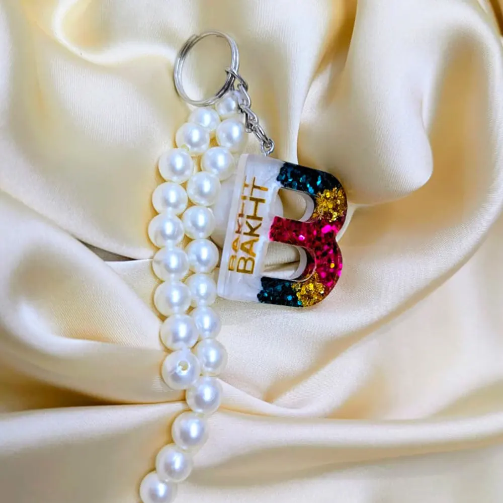 Personalized resin name keychain featuring a glitter letter B, custom name charm, and pearl beads on silk.