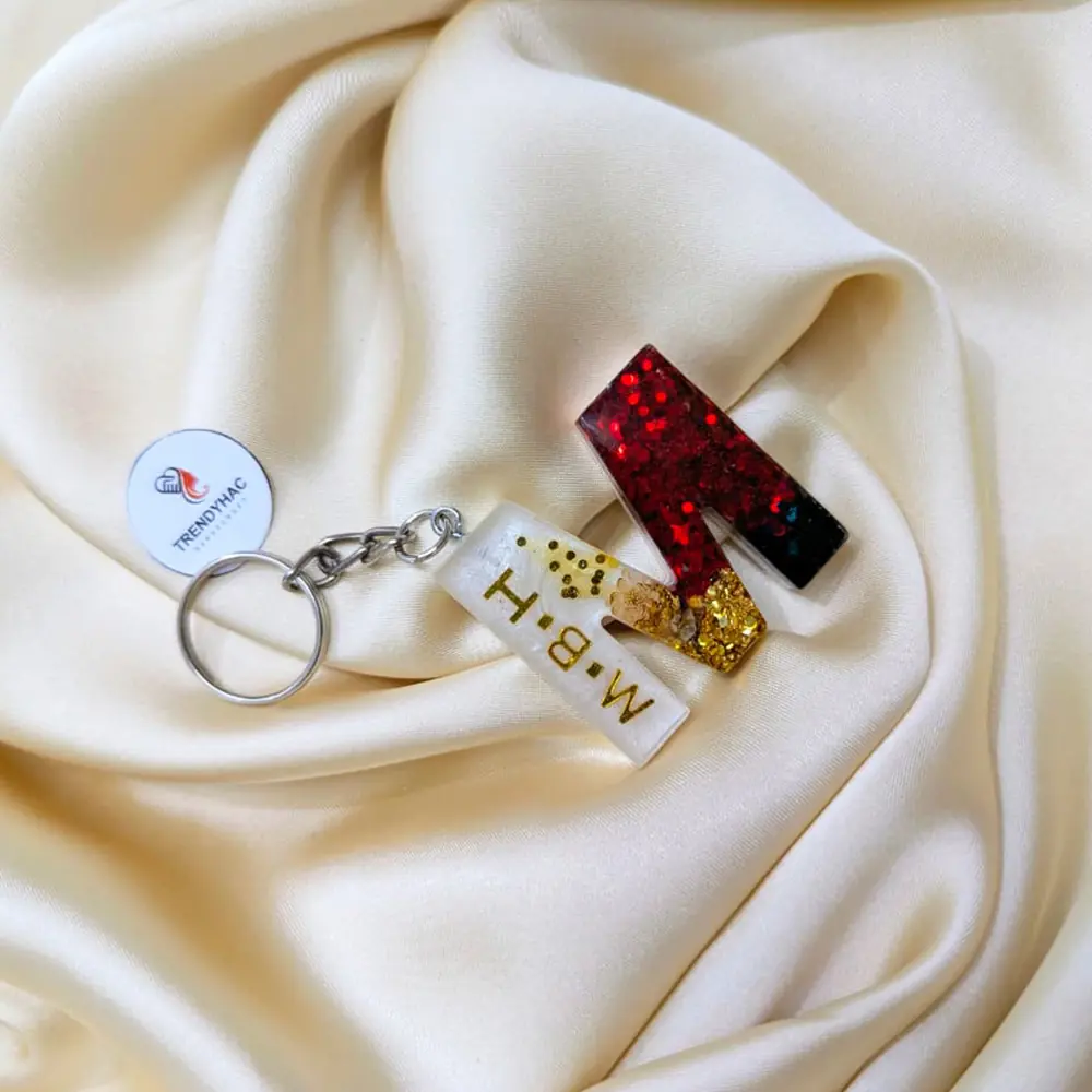 Handcrafted red glitter resin initial letter M keychain with gold foil bar charm on white silk background.
