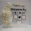 Full view of a transparent acrylic thumb impression board with gold lettering and a crescent border of white flowers.