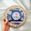 Handheld view of a circular blue resin newborn baby plaque with a central photo, birth stats, and a gold crystal geode border.