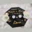 Flat lay view of a personalized black acrylic engagement ring tray with gold lettering, clear crystal ring boxes, and white roses.